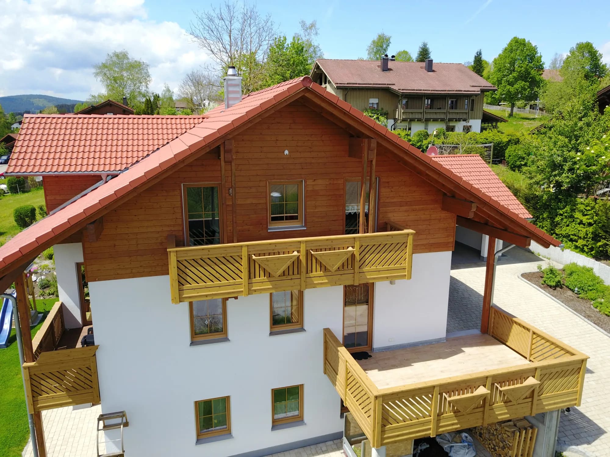 Front des Hauses mit Holzfassade, Balkonen und rotem Ziegeldach